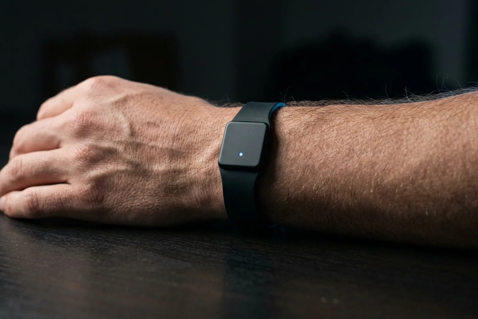 A plain matte-black wristband on a wrist, with a single small blue status light and no screen